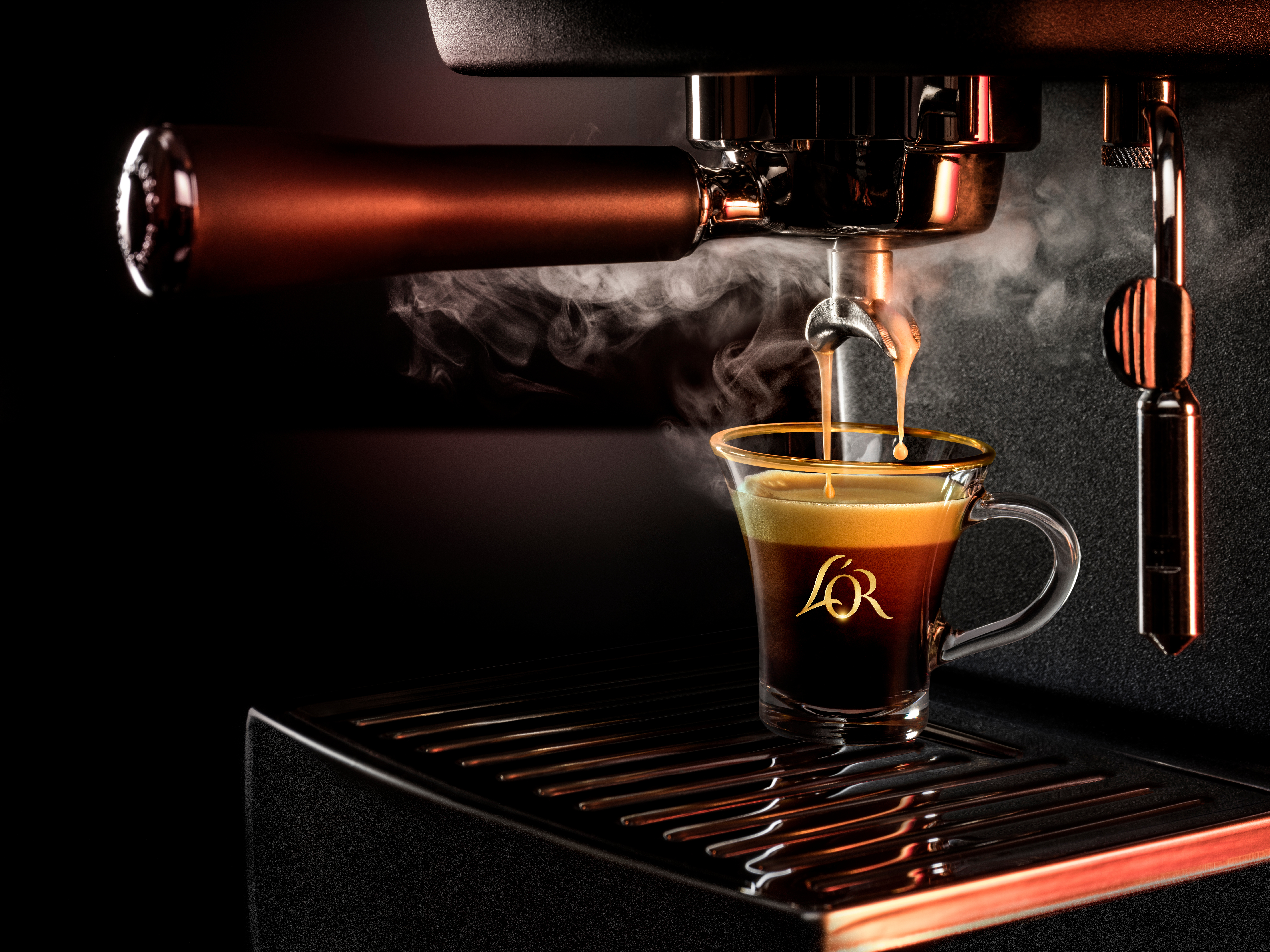 Tre pakker L'OR Espresso-kapsler med kaffekapsler og et glas espresso foran.