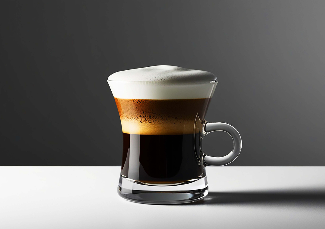 En kop sort kaffe i et glas med en mælkeskum står på et bord