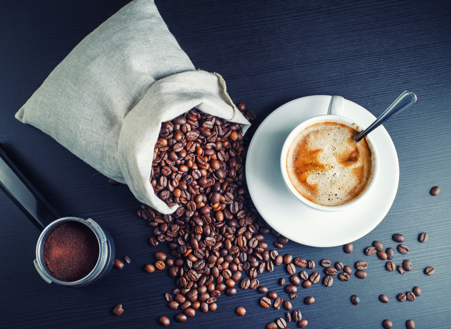 En kop kaffe på et bord med kaffebønner som bliver hældt ud fra en pose.
