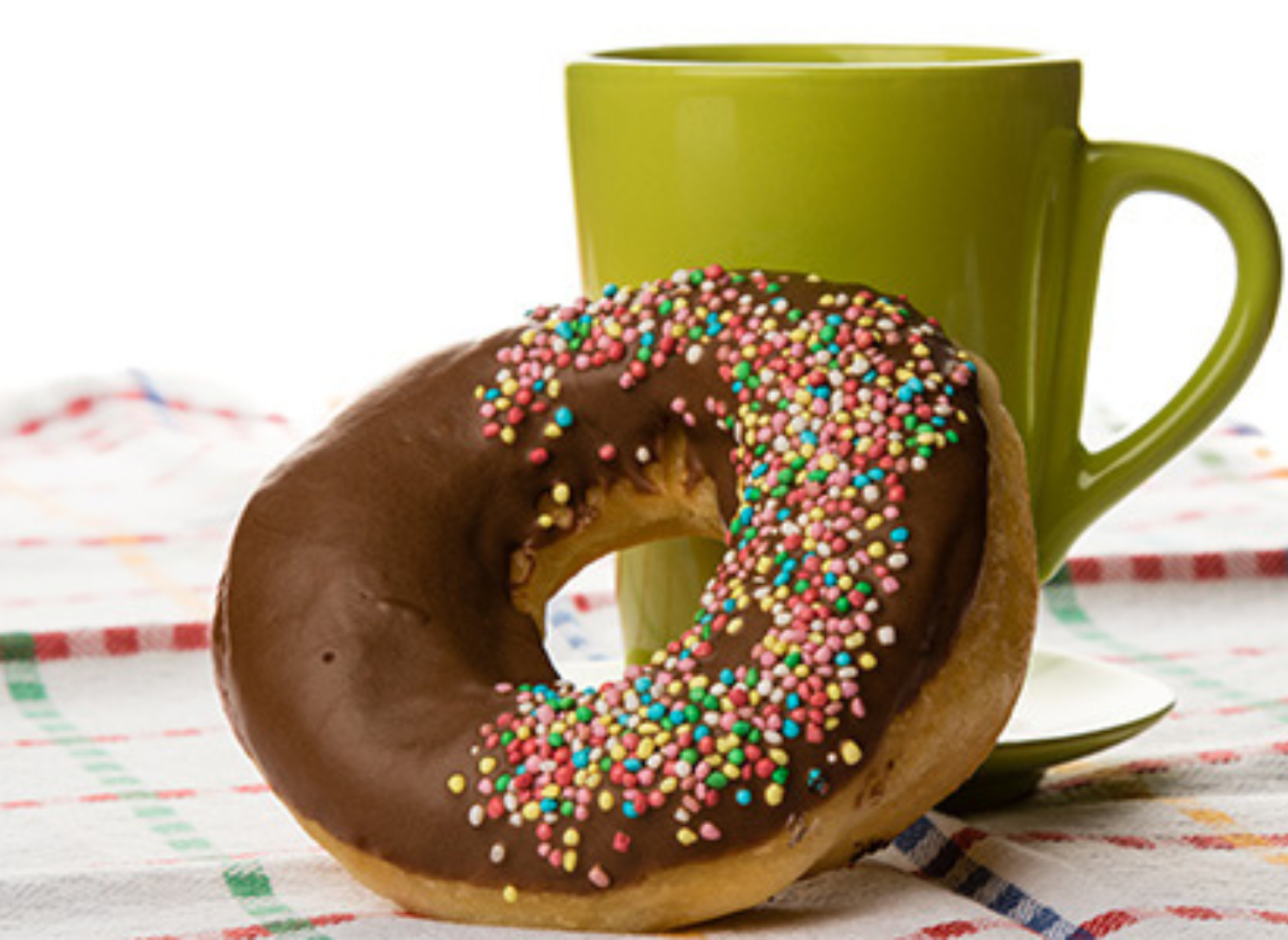 En donut med chokolade på et bord en grøn kop i baggrunden.