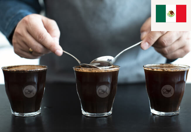 Tre kopper sort kaffe på et bord med mexicansk flag i højre hjørne