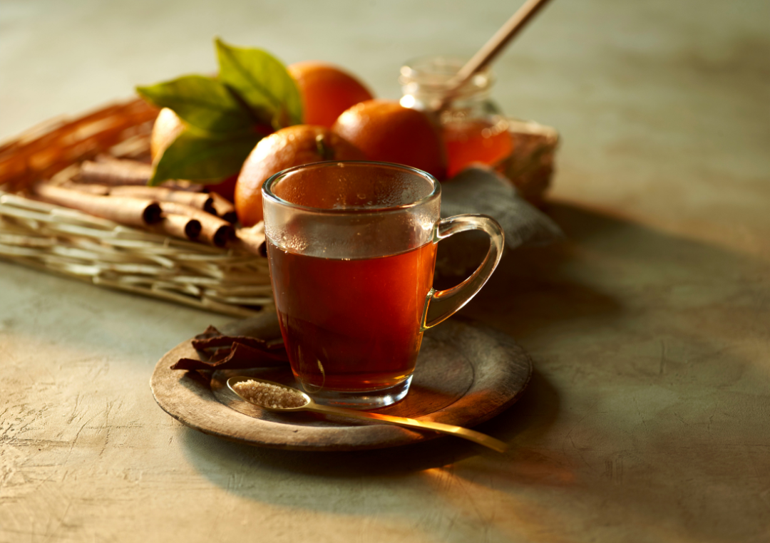 Rooibos te i en glaskop med mandariner i baggruden og en lille teske med sukker i.