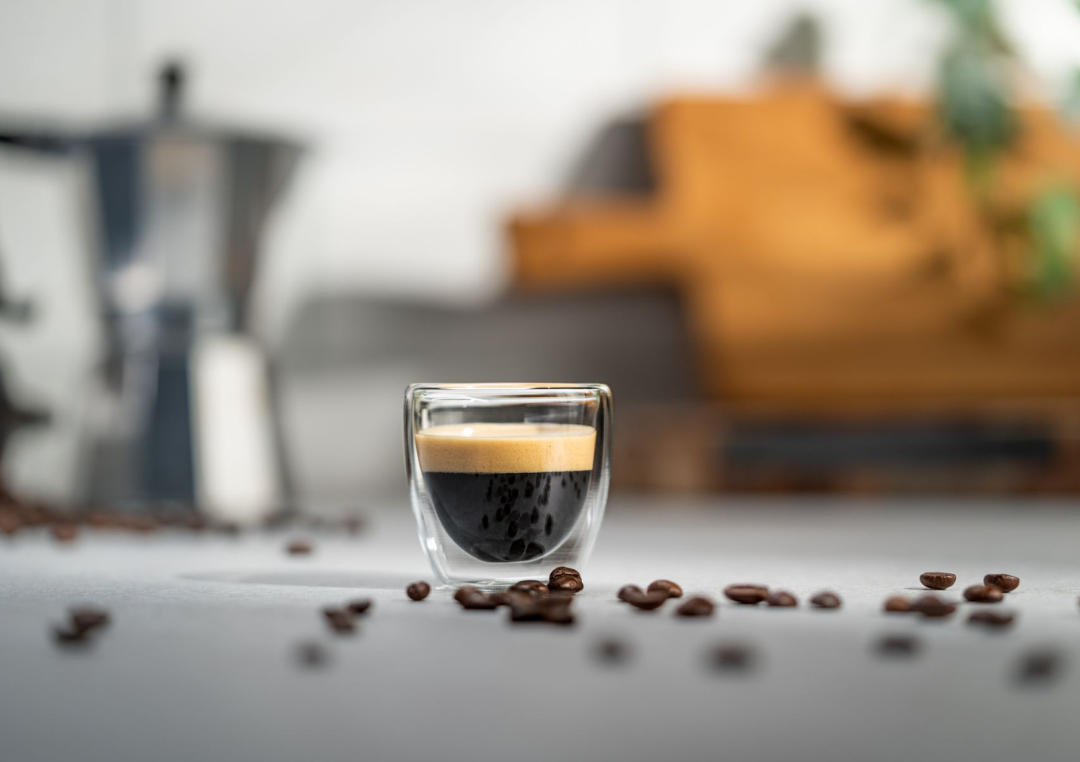 Kop espresso på et bord med et par kaffebønner liggende ved siden af.