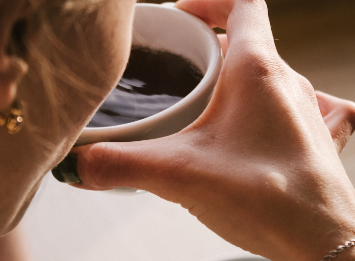Kvinde sidder med en sort kop kaffe i hånden