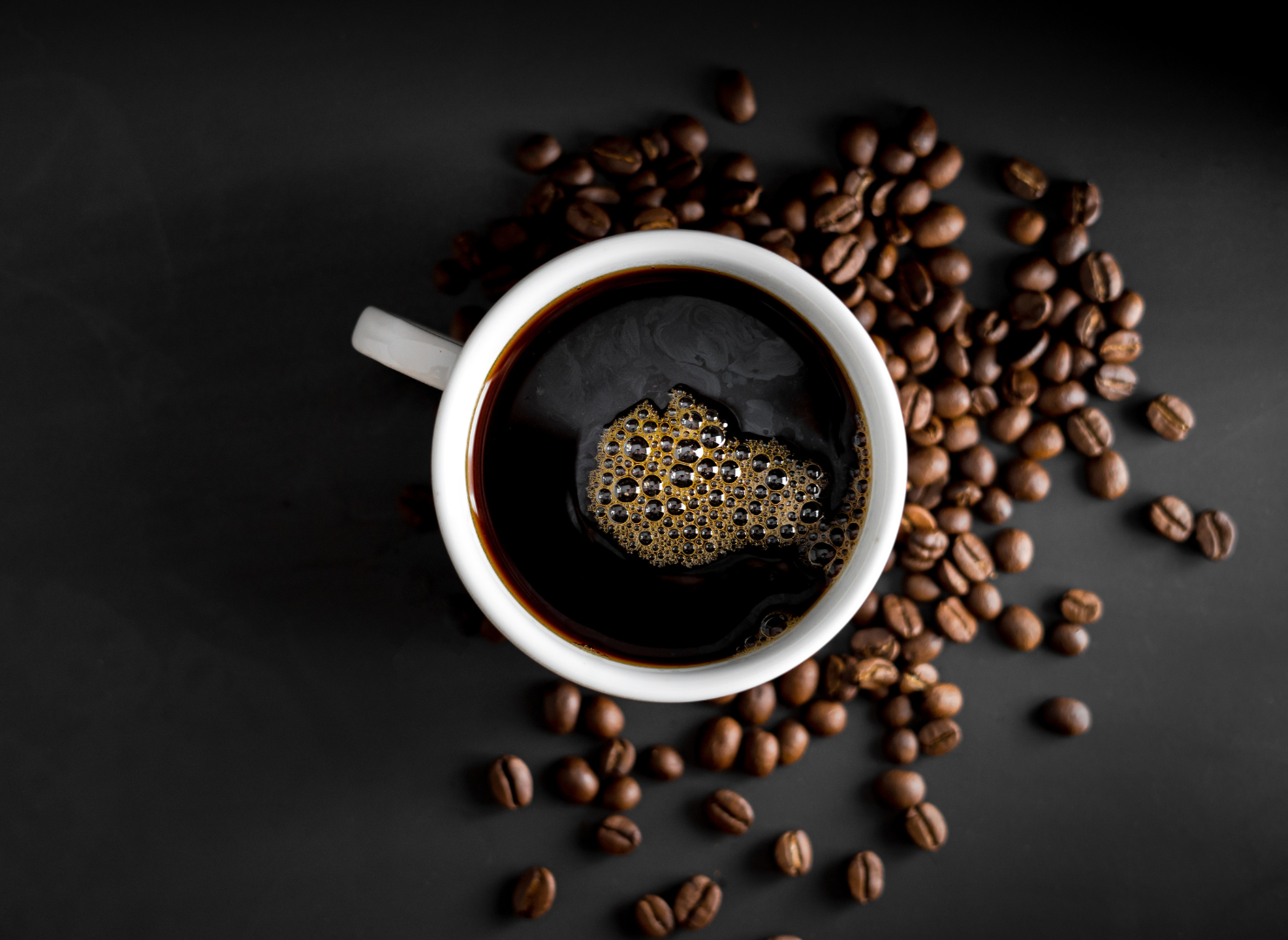 En kop sort kaffe set oppe fra med kaffebønner ved siden af.
