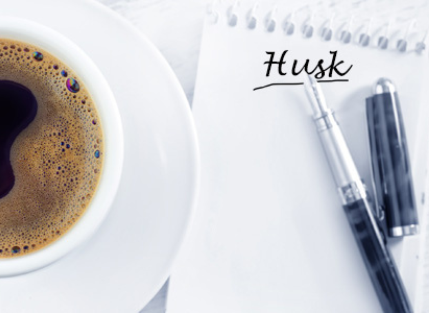 En kop kaffe på et bord med en notesblok og kuglepen ved siden af.