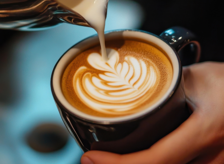 En kop med kaffe bliver hældt over med mælk for at lave et blad.