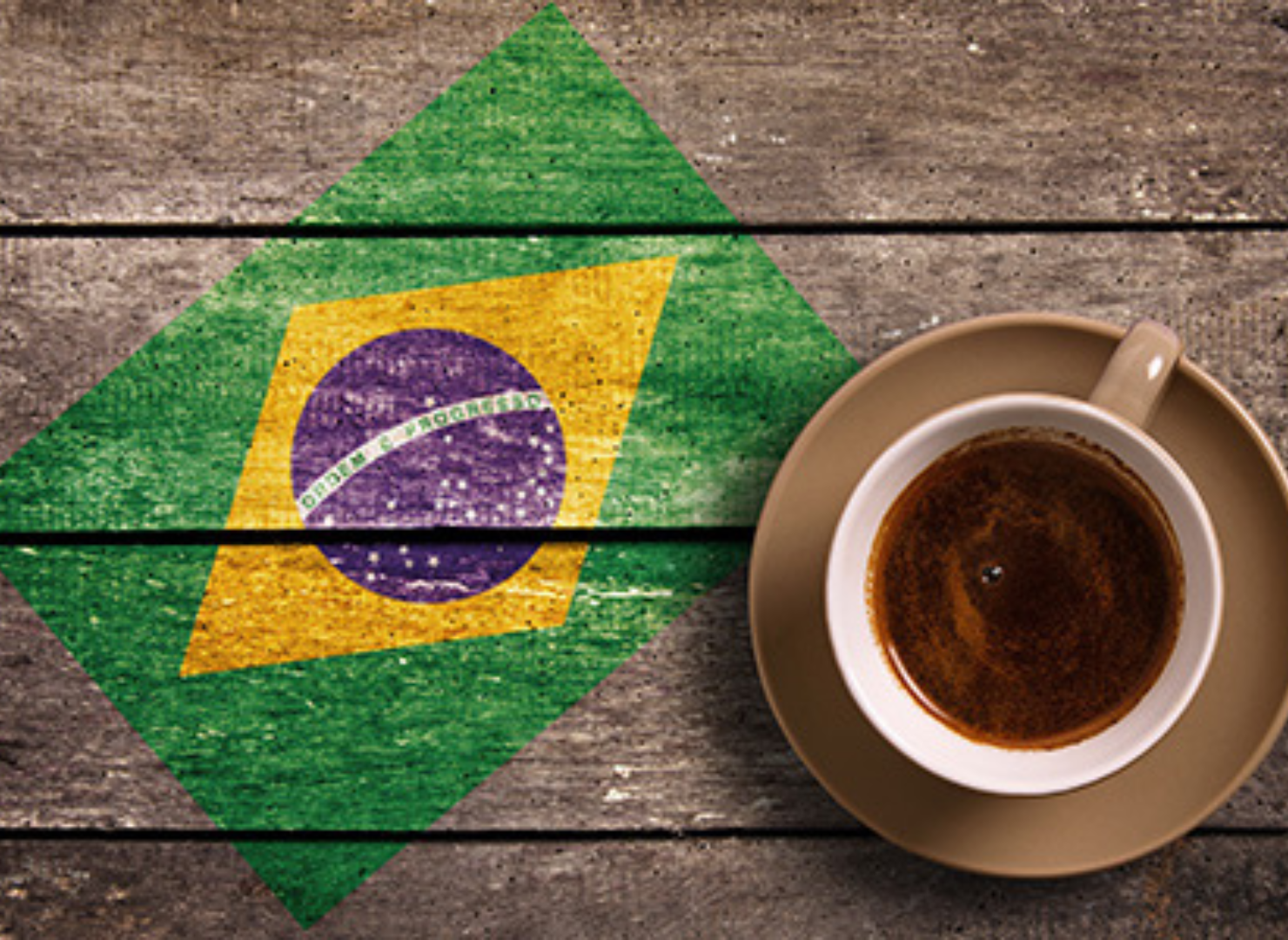 En kop kaffe set oppe fra på et træbord med det brasilianske flag malet henover.