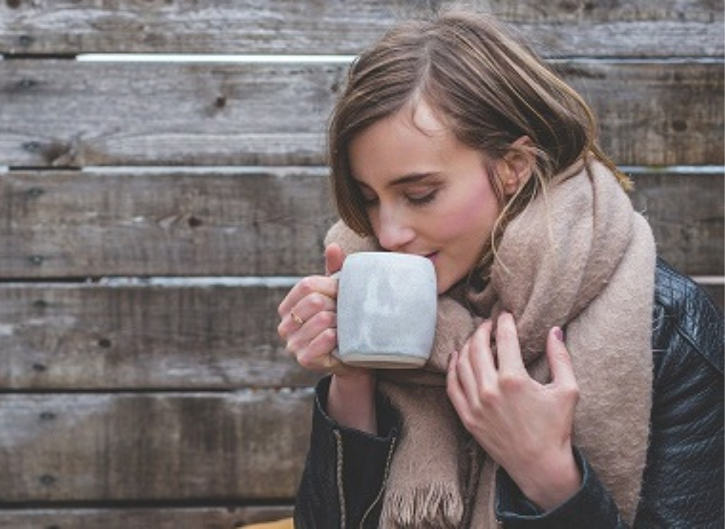 Kvinde med halstørklæde om halsen står udenfor med en kop kaffe i hånden.